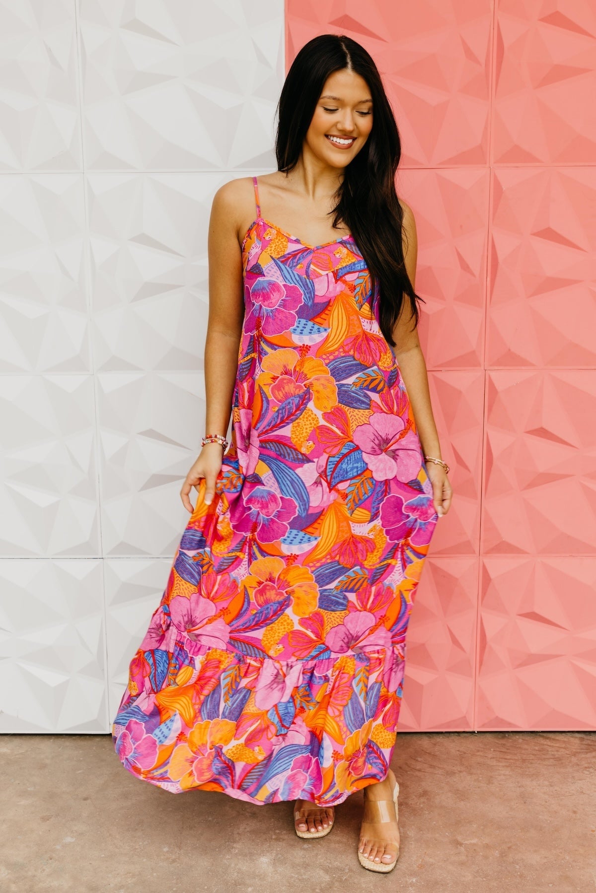Woman wearing a colorful floral dress against a white and pink textured wall.