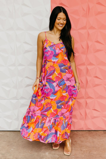Woman wearing a colorful floral dress against a white and pink textured wall.