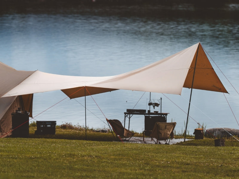 Kama Tarp beige and orange triangular canopy tent over grassy area near water