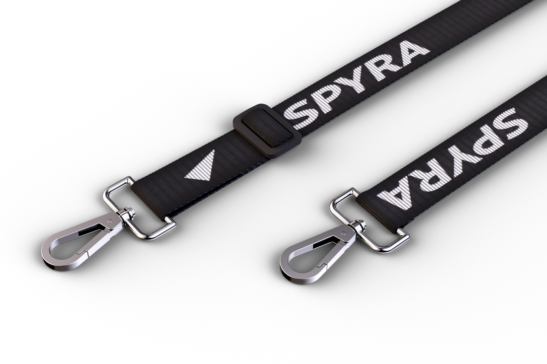 Partial SpyraStrap. Two bucklesand some part of the strap is visible.. The buckles are silver, the strap has a Spyra logo woven into it.