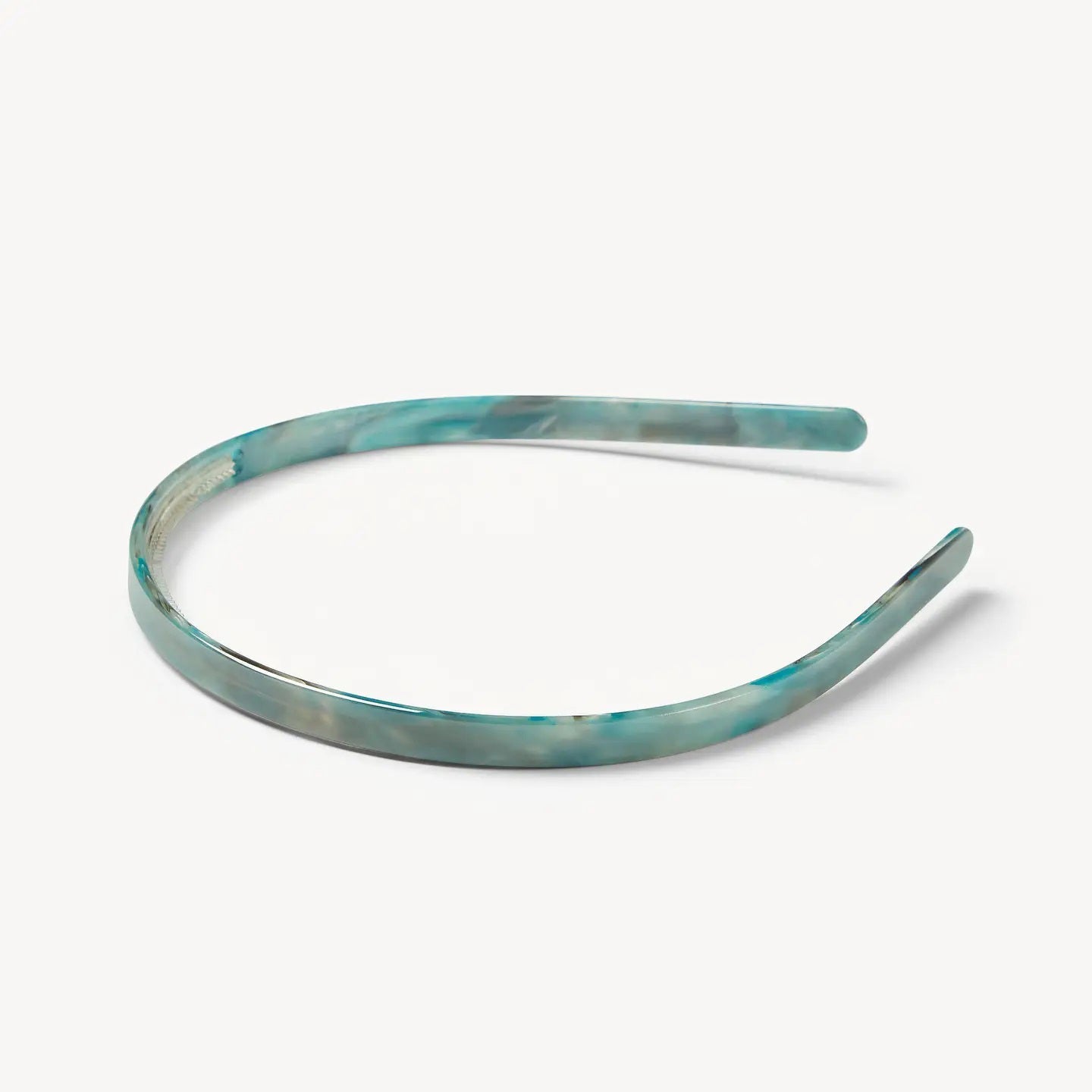 A young woman with wavy brown hair wears the MACHETE Ultralight Thin Headband in Jadeite and a gold hoop earring, gazing slightly past the camera with a neutral expression against a plain background.