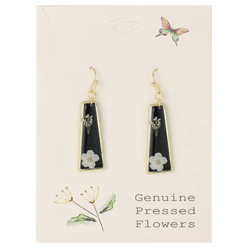 A pair of gold and black acrylic bar earrings with dried white flowers attached to them, displayed on a white card with illustrations of flowers.