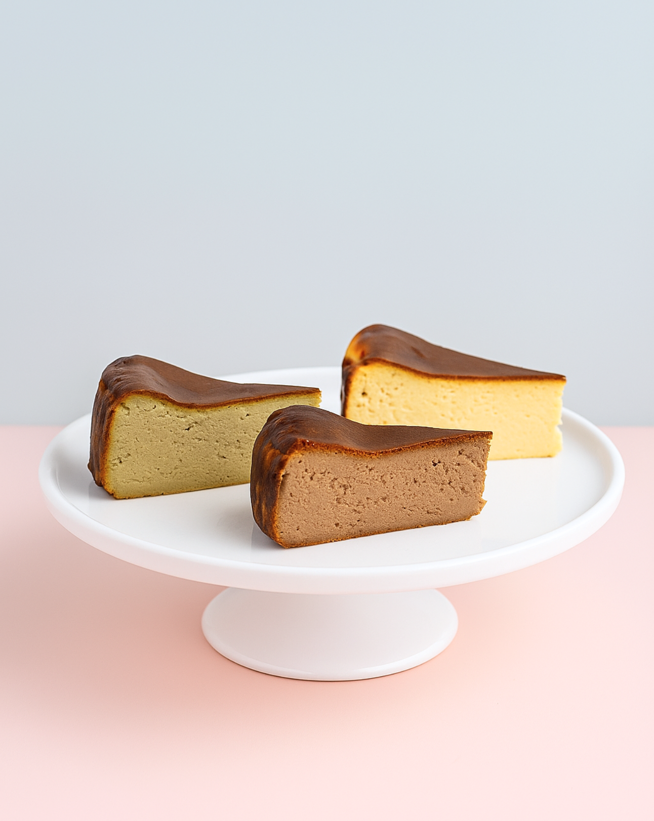Three slices of cheesecake on a white cake stand with a light gray background