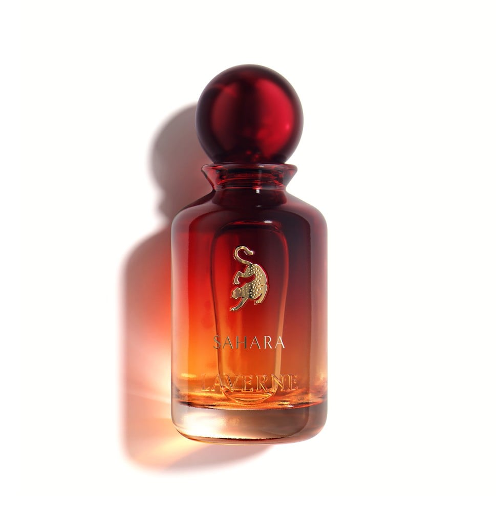 زجاجة عطر "صحارى" من لافيرن. الزجاجة تتدرج من الأحمر الداكن في الأعلى إلى البرتقالي/الكهرماني في الأسفل، محاكيةً ألوان غروب الشمس في الصحراء. الغطاء كروي وبلون أحمر داكن ولامع. الشعار الذهبي للافيرن (النمر الرابض) موجود في المنتصف، وتحته اسم "SAHARA" ثم "LAVERNE" باللون الذهبي.
