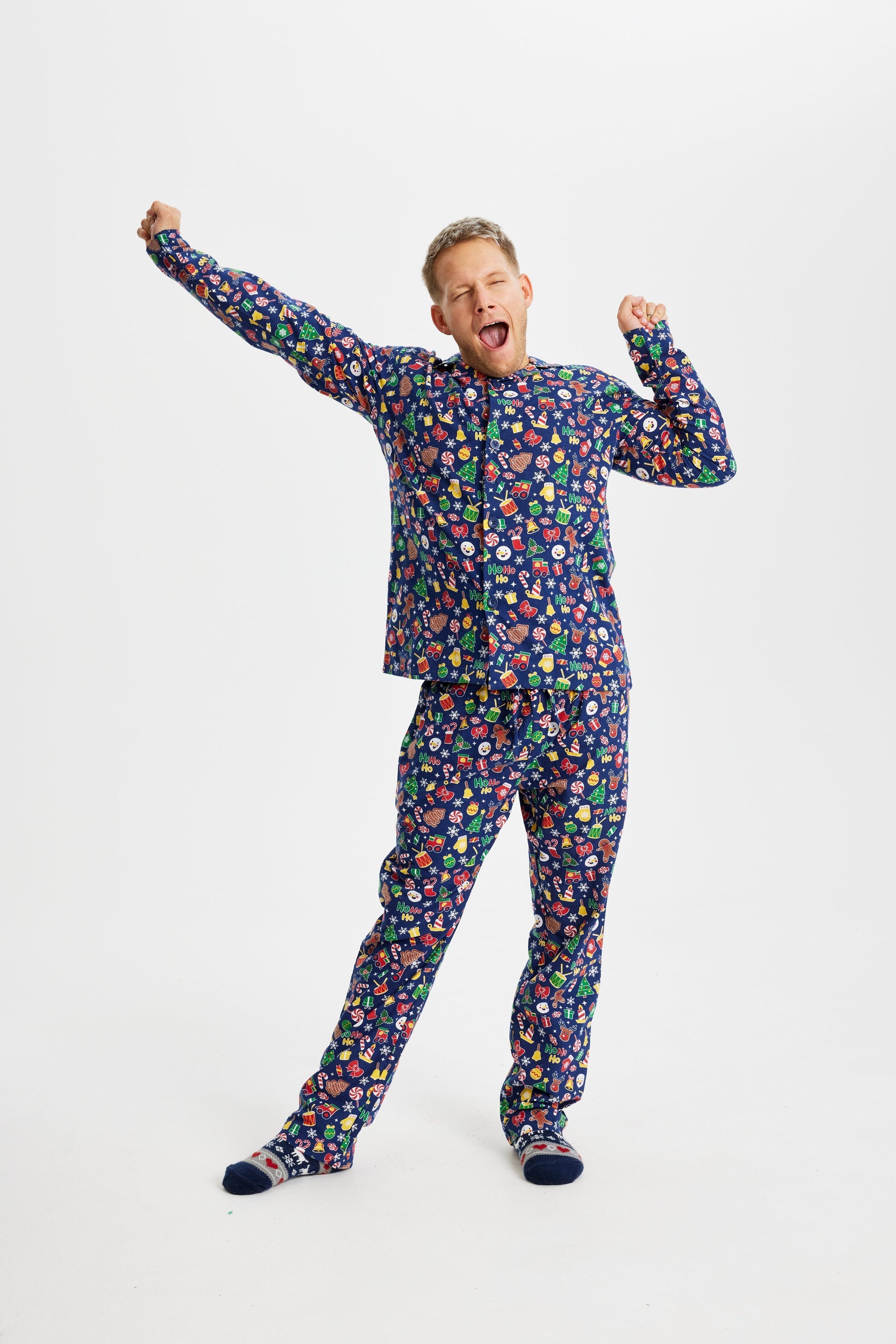 En gäspande man klädd i en blå julpyjamas med julprylar.