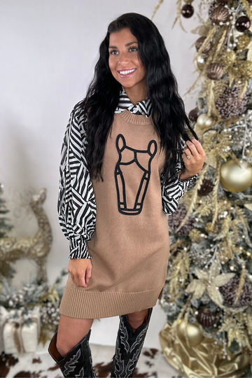 Woman wearing a horse sweater with a graphic design in front of a decorated Christmas tree.