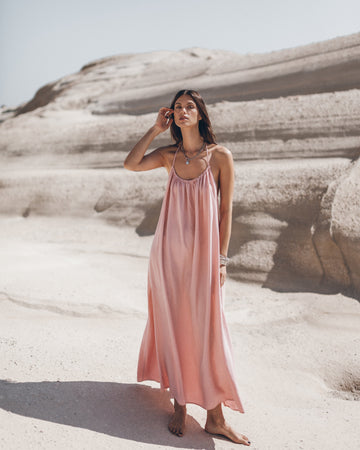 Woman in a pink dress standing on a sandy beach with sand dunes in the background