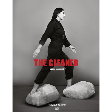 Eine Schwarz-Weiß-Fotografie von Marina Abramović, die in einem dunklen Overall barfuß über zwei große, helle Kristalle geht. In roten Großbuchstaben steht der Titel THE CLEANER über dem Bild.