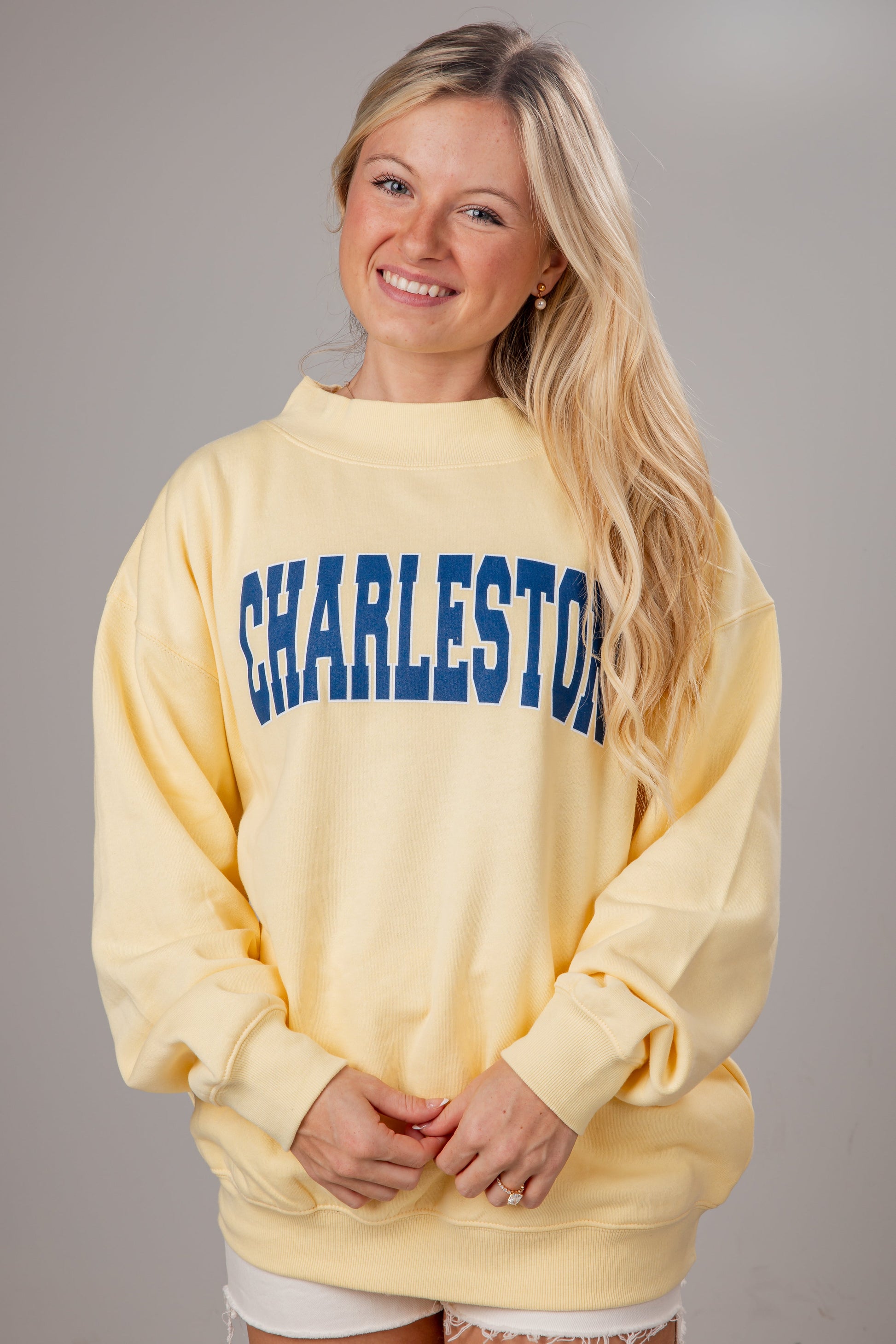 Woman wearing a yellow sweatshirt with 'Charleston' printed in blue on a gray background