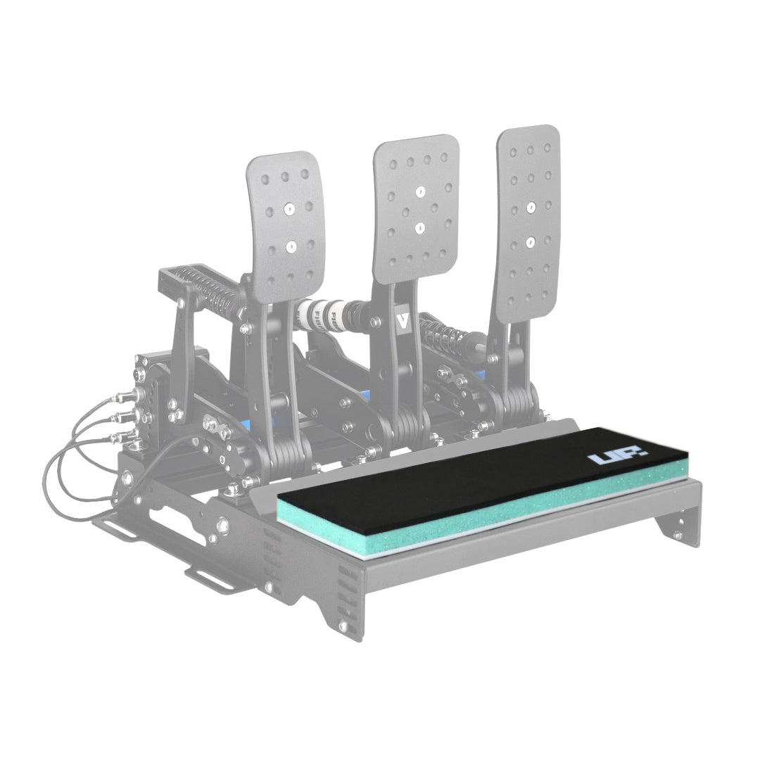A black multi-layer cushion, the Unreal Racing HeelPad, mounted on a racing pedal setup, designed for barefoot sim racing.