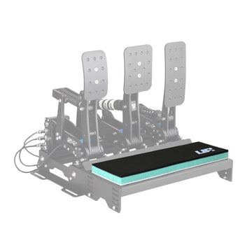 A black multi-layer cushion, the Unreal Racing HeelPad, mounted on a racing pedal setup, designed for barefoot sim racing.